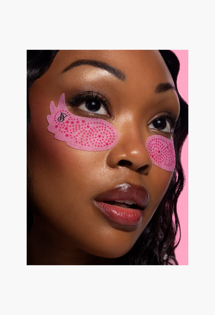 GLAM MODA Victoria's Secret x Patchology pink wing-shaped hydrating eye patches applied on a model's under-eye area.