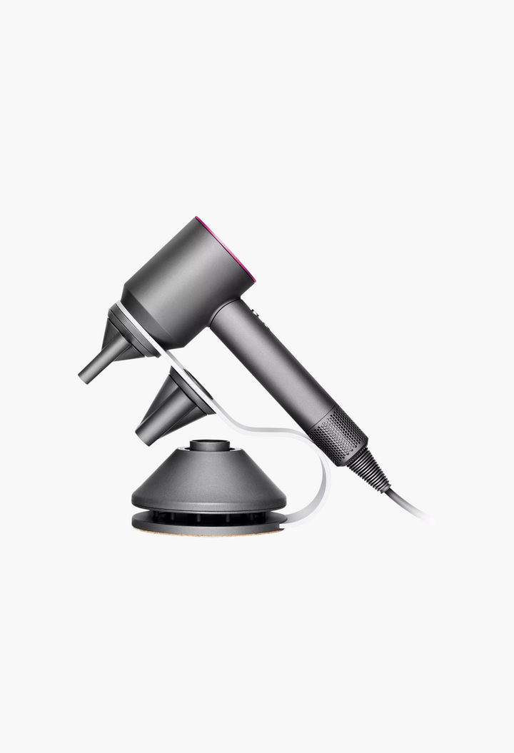 GLAM MODA Dyson Supersonic hair dryer in grey with pink accent, resting on a sleek display stand with attachments