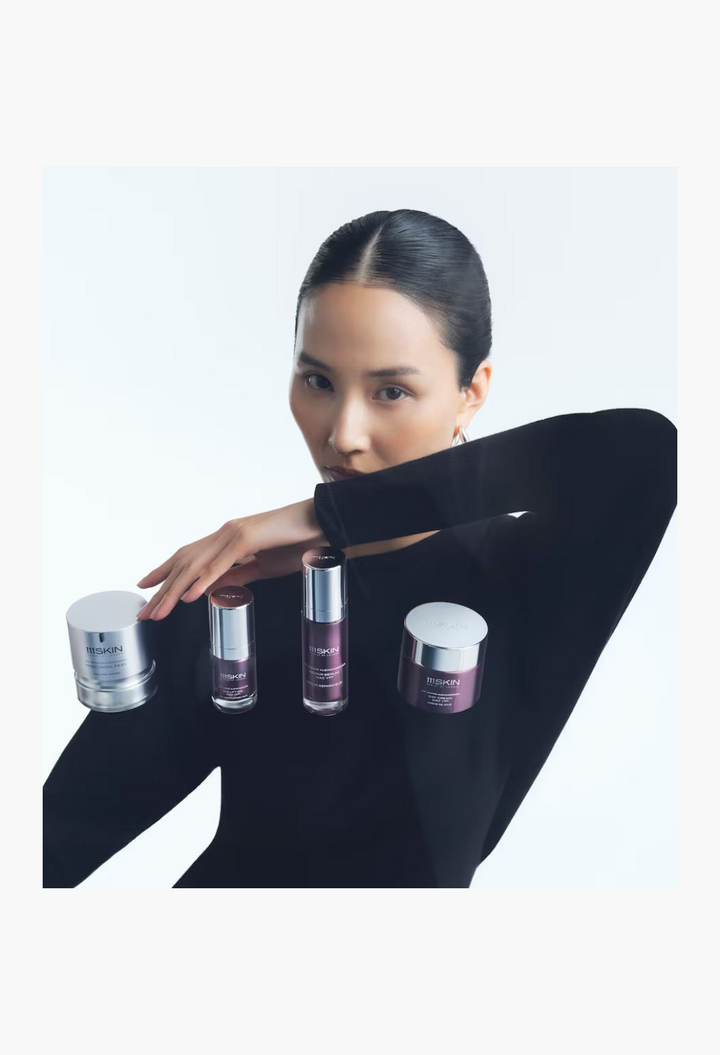 GLAM MODA model posing with 111SKIN Precision Peel and skincare products in sleek silver and purple packaging