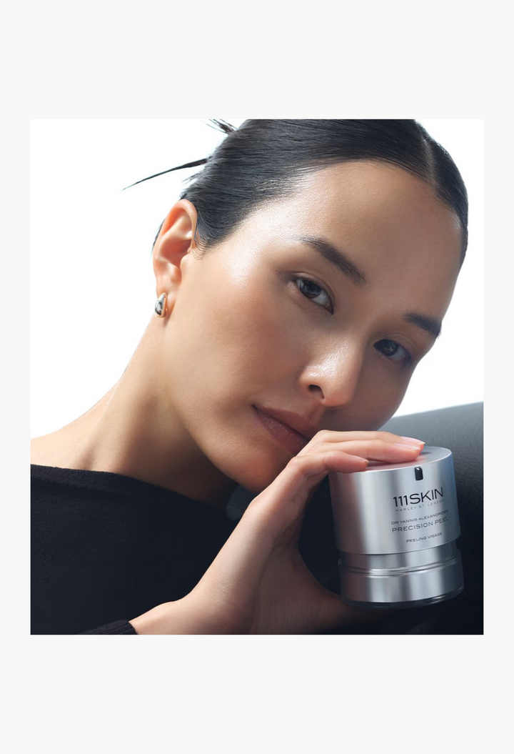 GLAM MODA model holding a silver 111SKIN Precision Peel jar, showcasing a radiant complexion and skincare product.