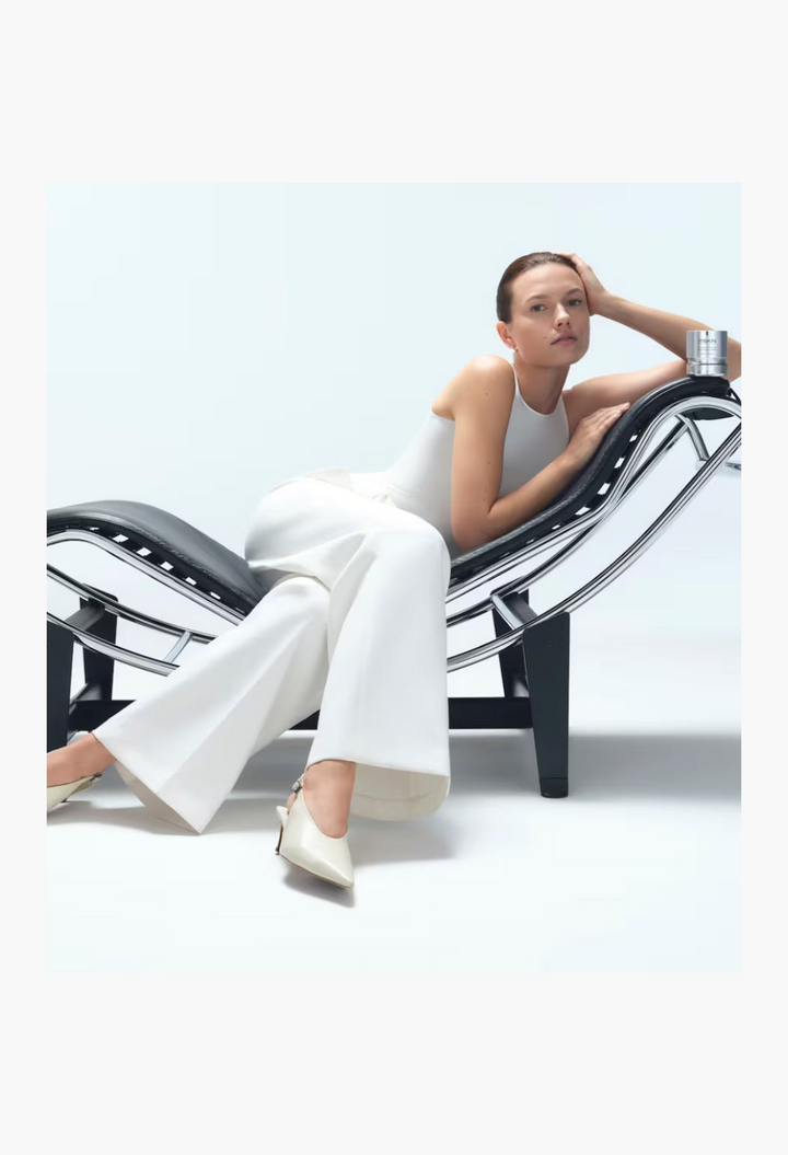 GLAM MODA Precision Peel skincare product placed on a modern black lounge chair next to a woman in white attire.