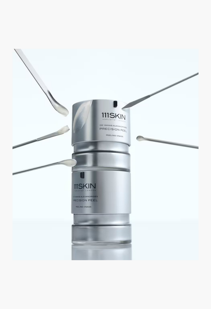 GLAM MODA 111SKIN Precision Peel resurfacing treatment in a silver bottle surrounded by four small applicator spatulas.