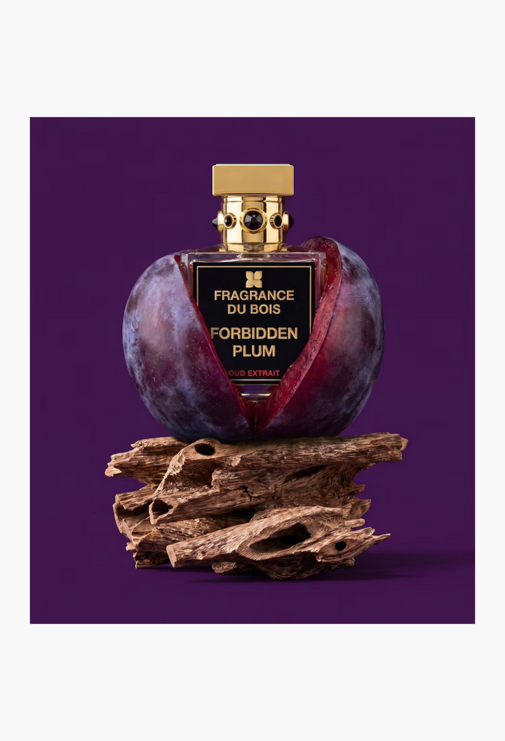 GLAM MODA Fragrance Du Bois Forbidden Plum Oud Extrait perfume bottle nestled in a plum on a piece of driftwood.
