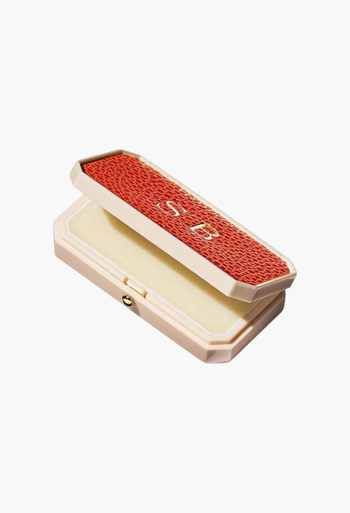 GLAM MODA Baume des Muses Ivory lip balm in a rectangular case with a textured orange lid and gold embossed initials.