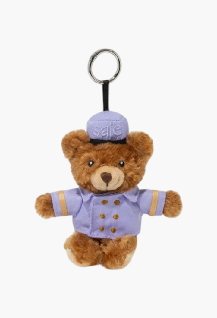 GLAM MODA brown plush bear keychain wearing a purple bellhop uniform with a matching cap and gold button details.