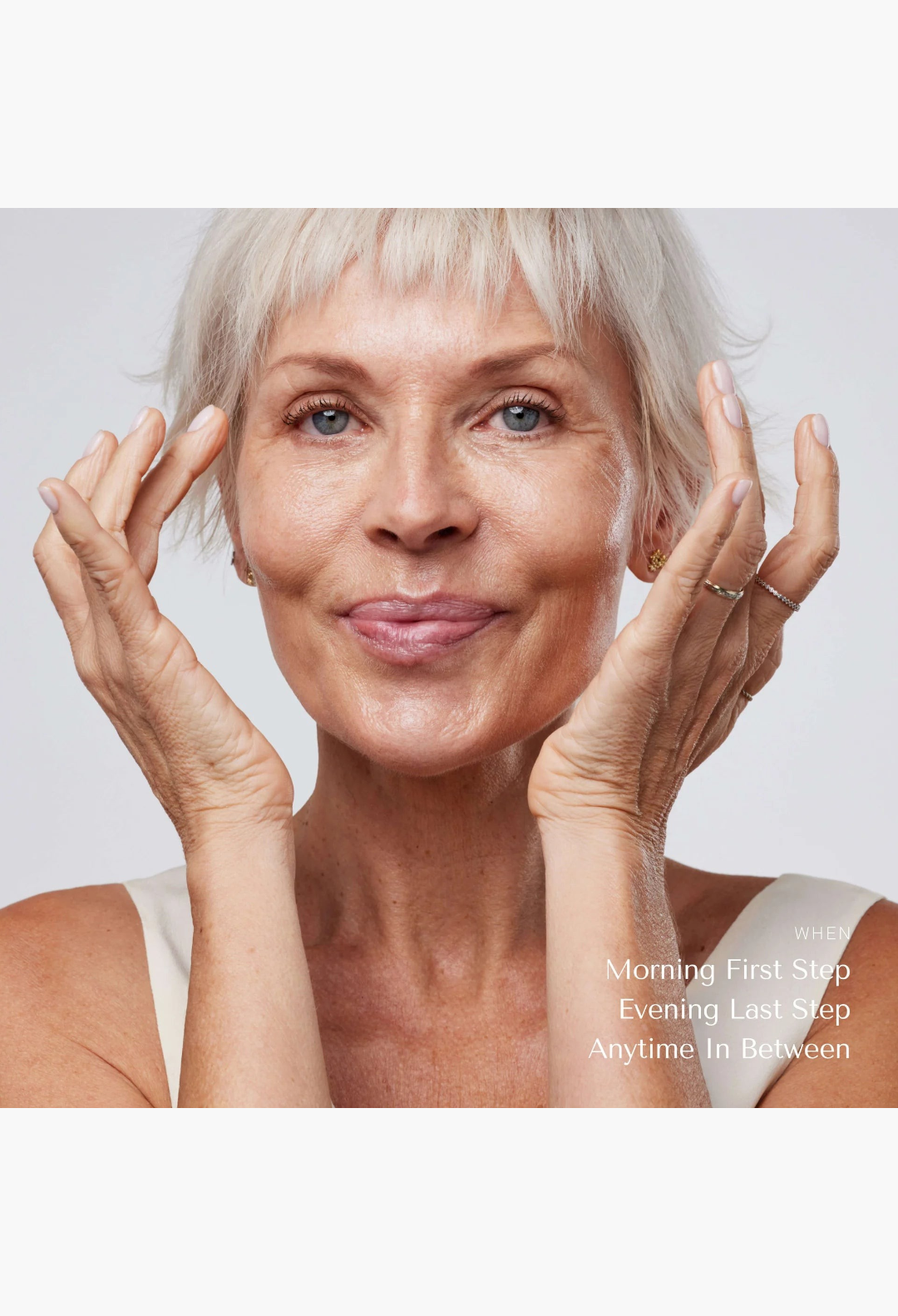 GLAM MODA mature woman with short silver hair applying solid serum to her face for radiant and nourished skin