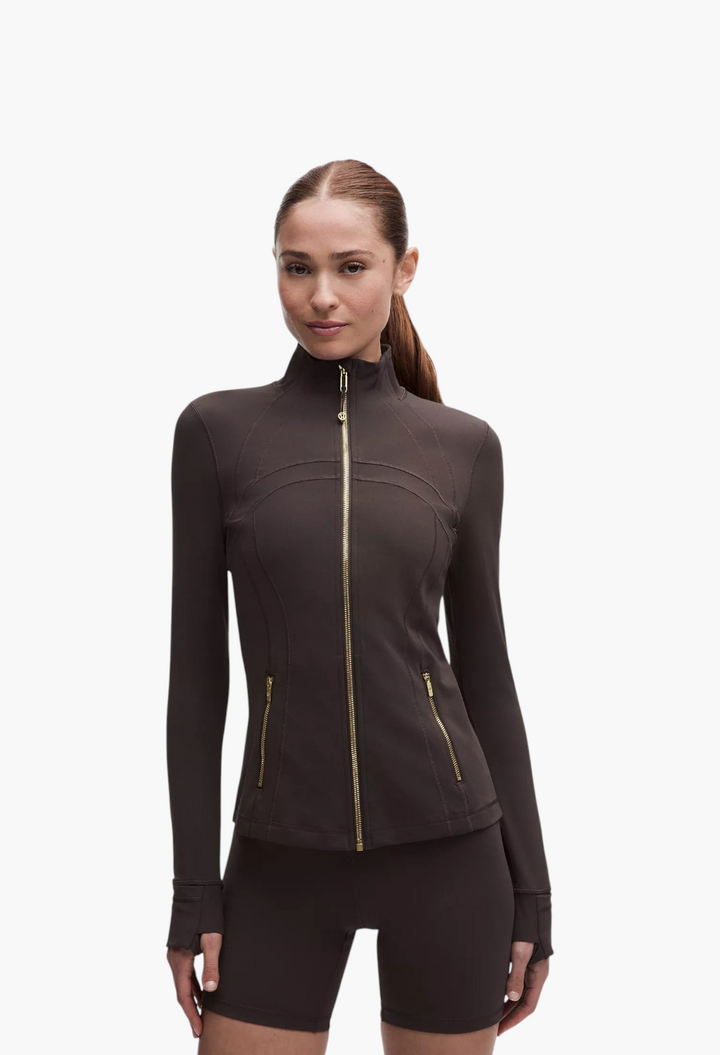 GLAM MODA Define Jacket Nulu in dark brown, featuring a slim fit, zippered pockets, and thumbholes on a model.