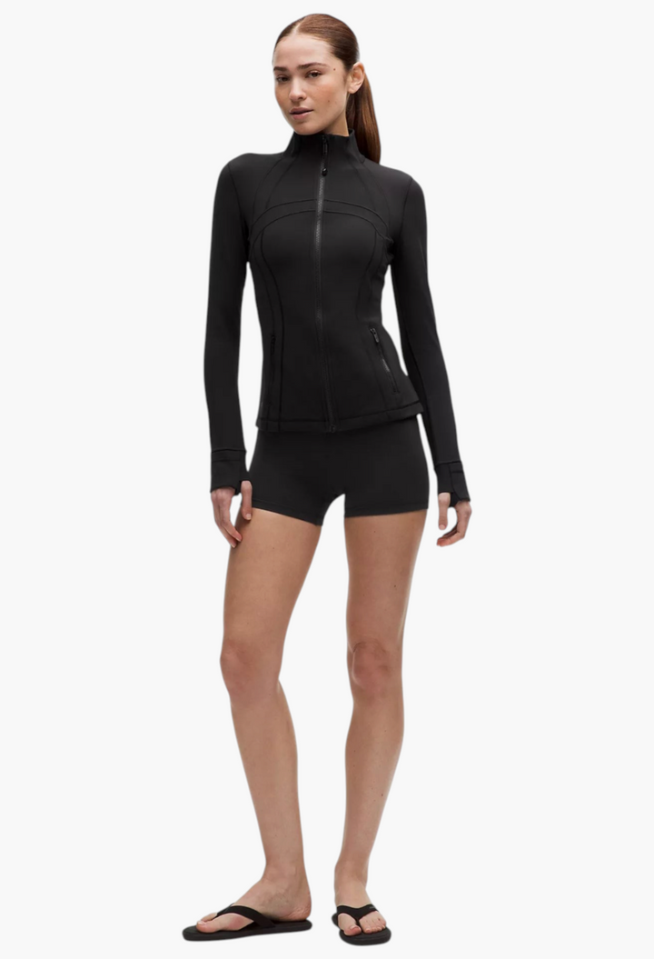 Model wearing GLAM MODA black Define Jacket Nulu with thumbholes, zippered pockets, and slim fit design.