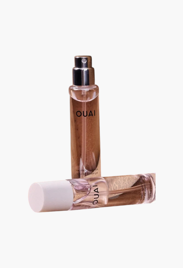 GLAM MODA travel-sized OUAI Laurel Canyon Eau de Parfum spray bottles resting on a textured tan leather surface.
