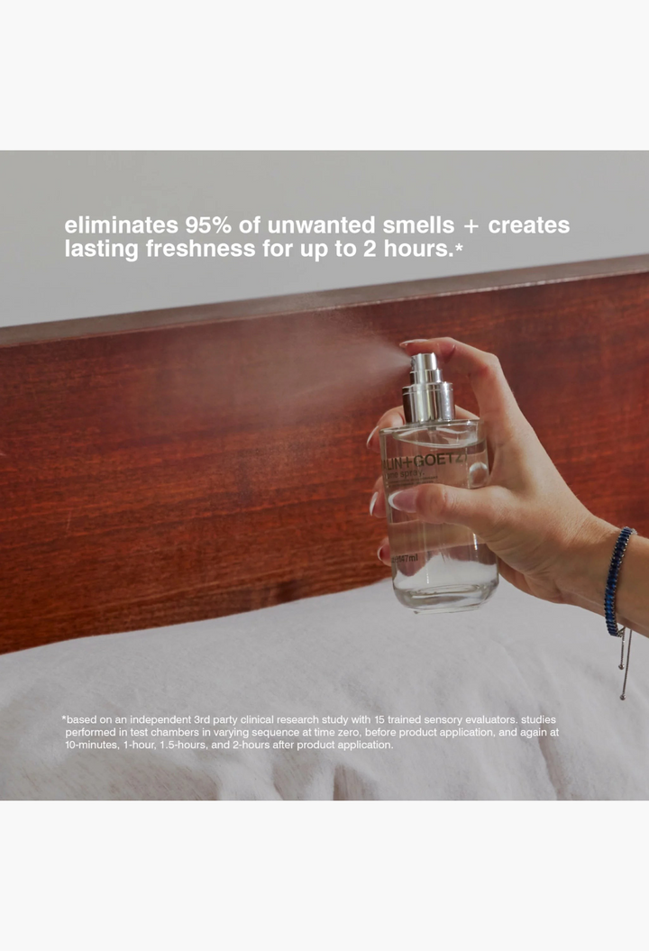 GLAM MODA Otto alcohol-free home spray in a clear glass bottle held by a hand wearing a blue beaded bracelet.