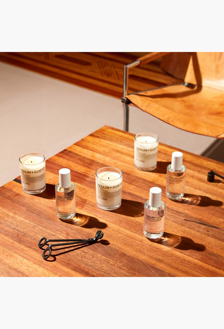 GLAM MODA collection of Malin + Goetz Otto home sprays and candles with a black metal wick trimmer on a white background