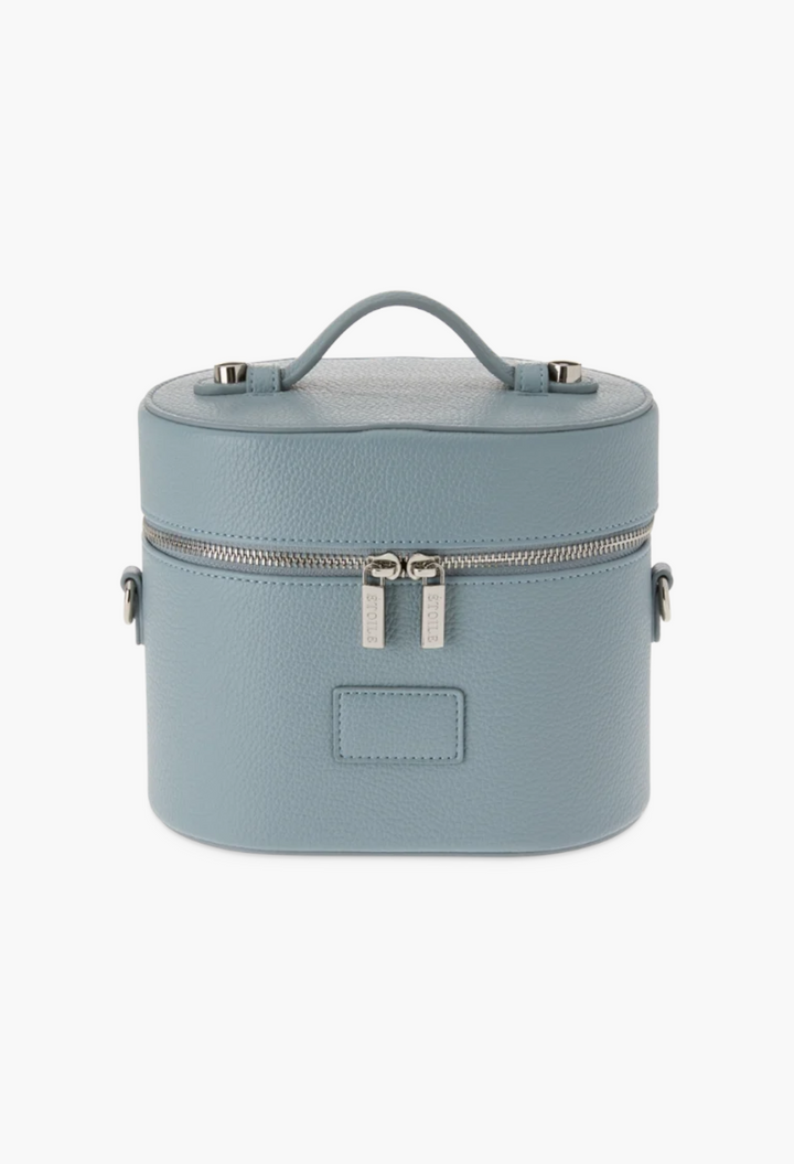 GLAM MODA oval toiletry case in dusty blue vegan leather with a top handle, dual zippers, and a structured design.