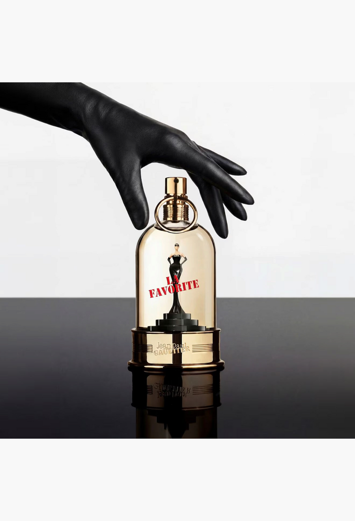 GLAM MODA Jean Paul Gaultier La Favorite Eau de Parfum in a unique pedestal bottle held by a hand in a black glove.
