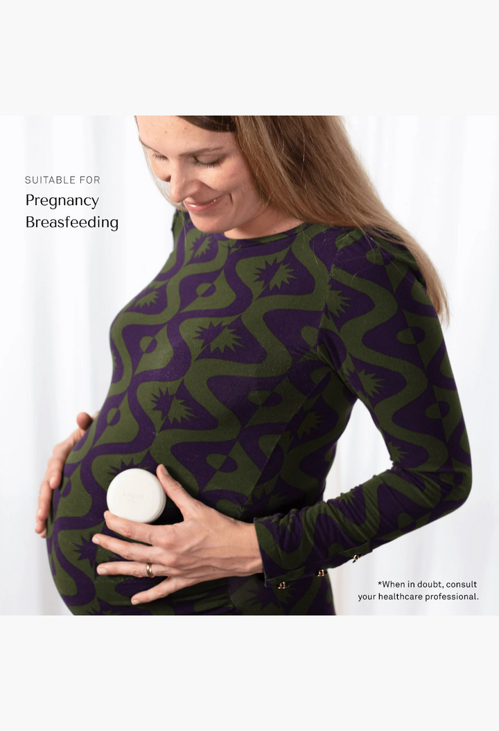 GLAM MODA Le Balm solid serum held by a pregnant woman wearing a green and purple patterned long-sleeve dress