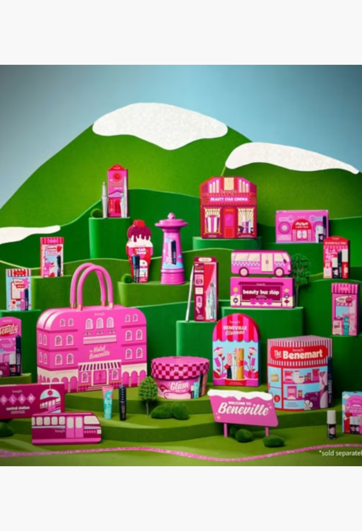 GLAM MODA Benefit The Hotel Beneville 24-piece beauty advent calendar featuring pink makeup boxes in a whimsical town.