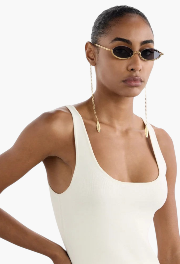 Model wearing GLAM MODA Gaga gold metal sculptural sunglasses with dangling feather-like jewelry chain details.