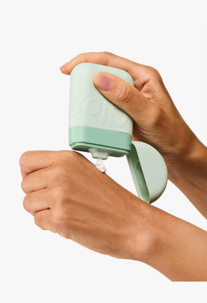 GLAM MODA fast-absorbing hand cream in a light green palm-sized squeeze pod being applied to the back of a hand.