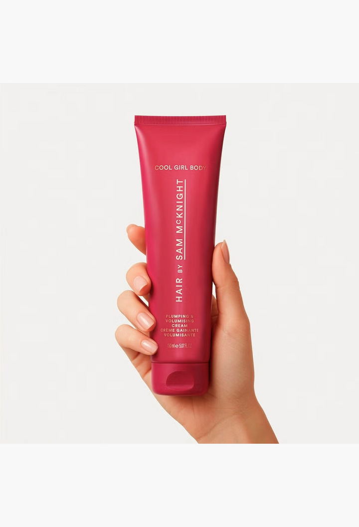 GLAM MODA Hair By Sam McKnight Cool Girl Body Volumising & Plumping Cream in a pink squeeze tube held in a hand.