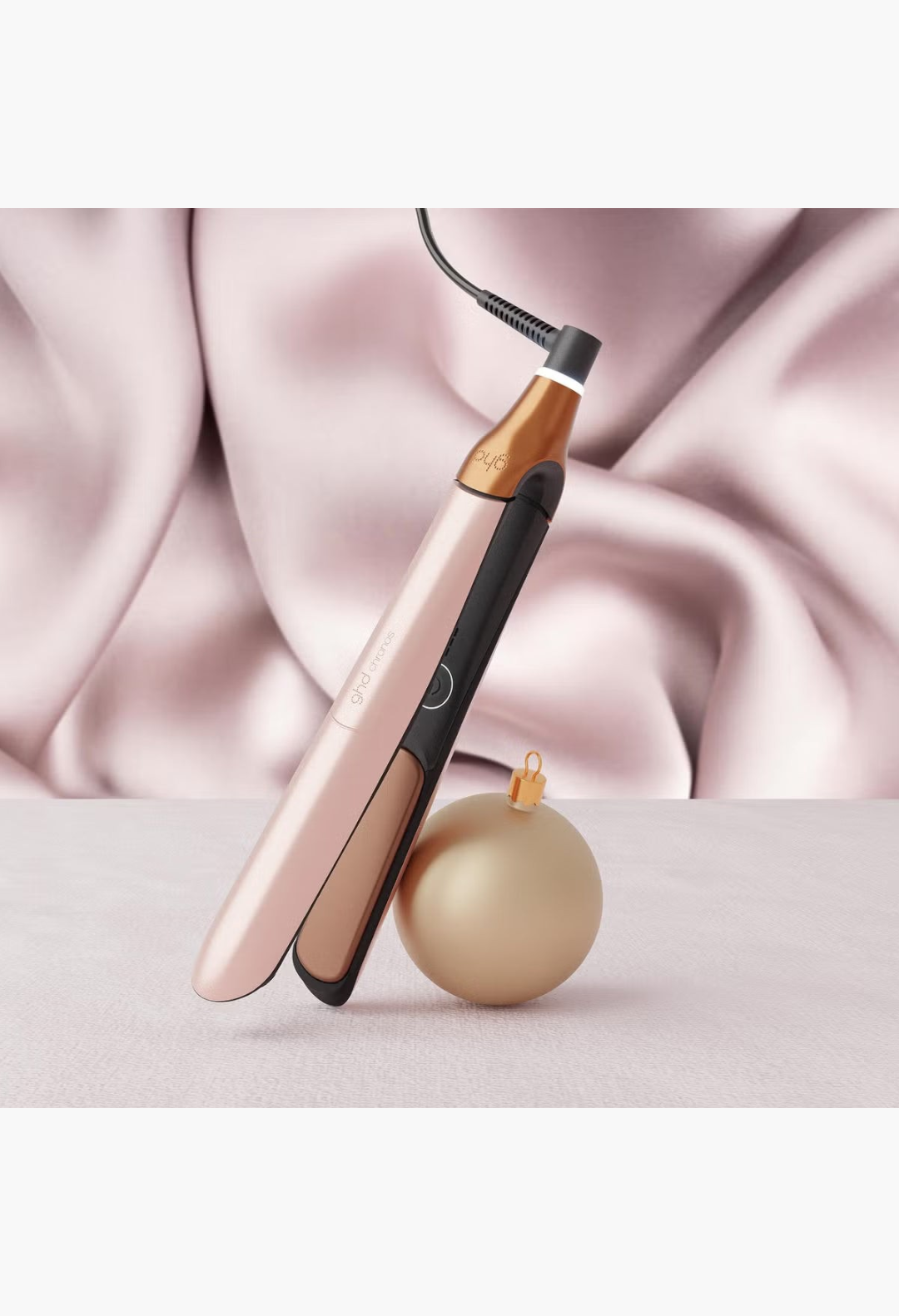 GLAM MODA ghd Chronos hair straightener in metallic rose gold with a matching Christmas ornament on a white background