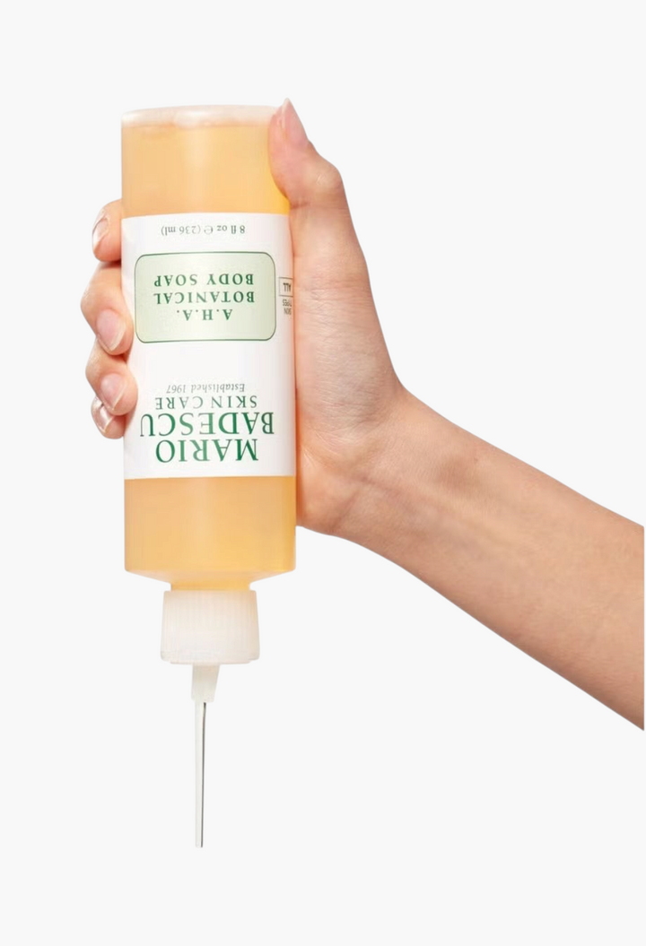 GLAM MODA Mario Badescu AHA Botanical Body Soap in a clear bottle being held and squeezed to dispense product