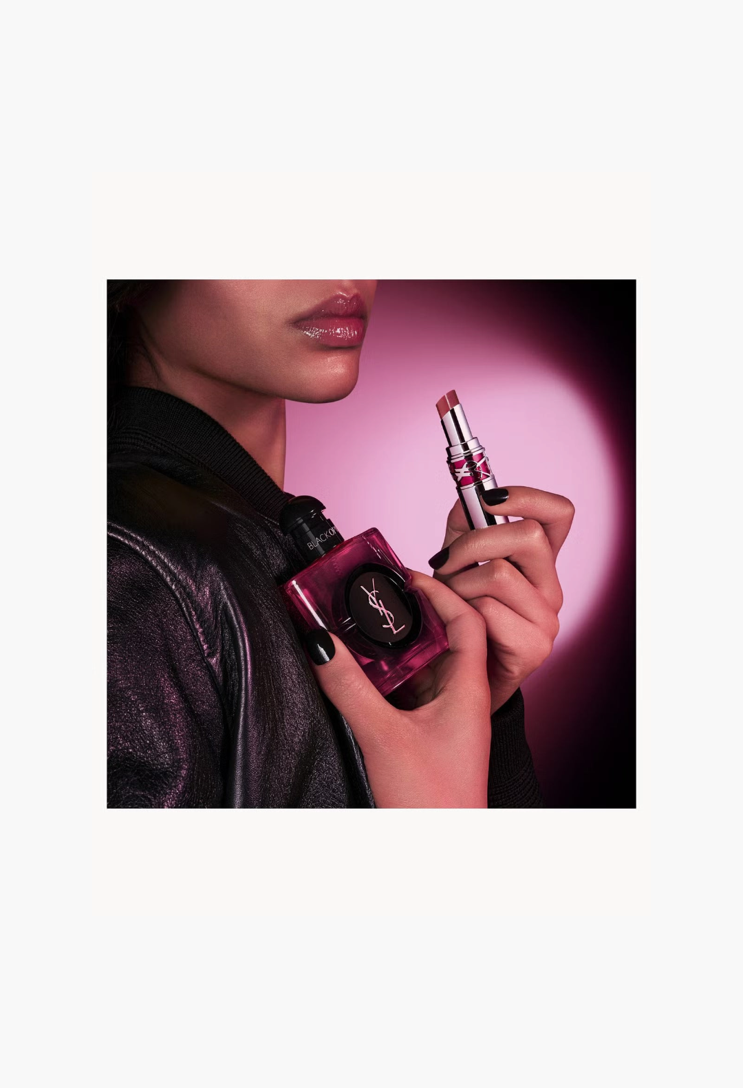 GLAM MODA model holding YSL Black Opium Pink Glaze perfume bottle and matching lipstick in a dark, stylish setting.