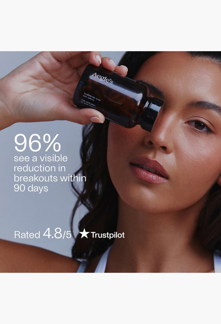 GLAM MODA model holding a brown glass bottle of Aegle Clear Skin Complex supplement near her face