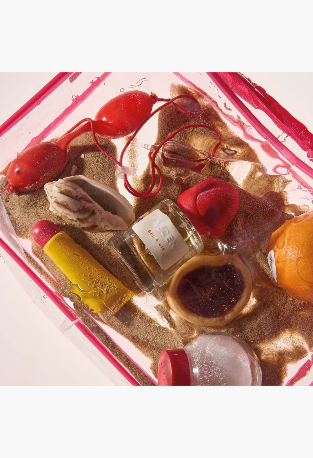 GLAM MODA Fascent Sel À Vie perfume bottle surrounded by sand, seashells, and citrus fruits in a clear pouch