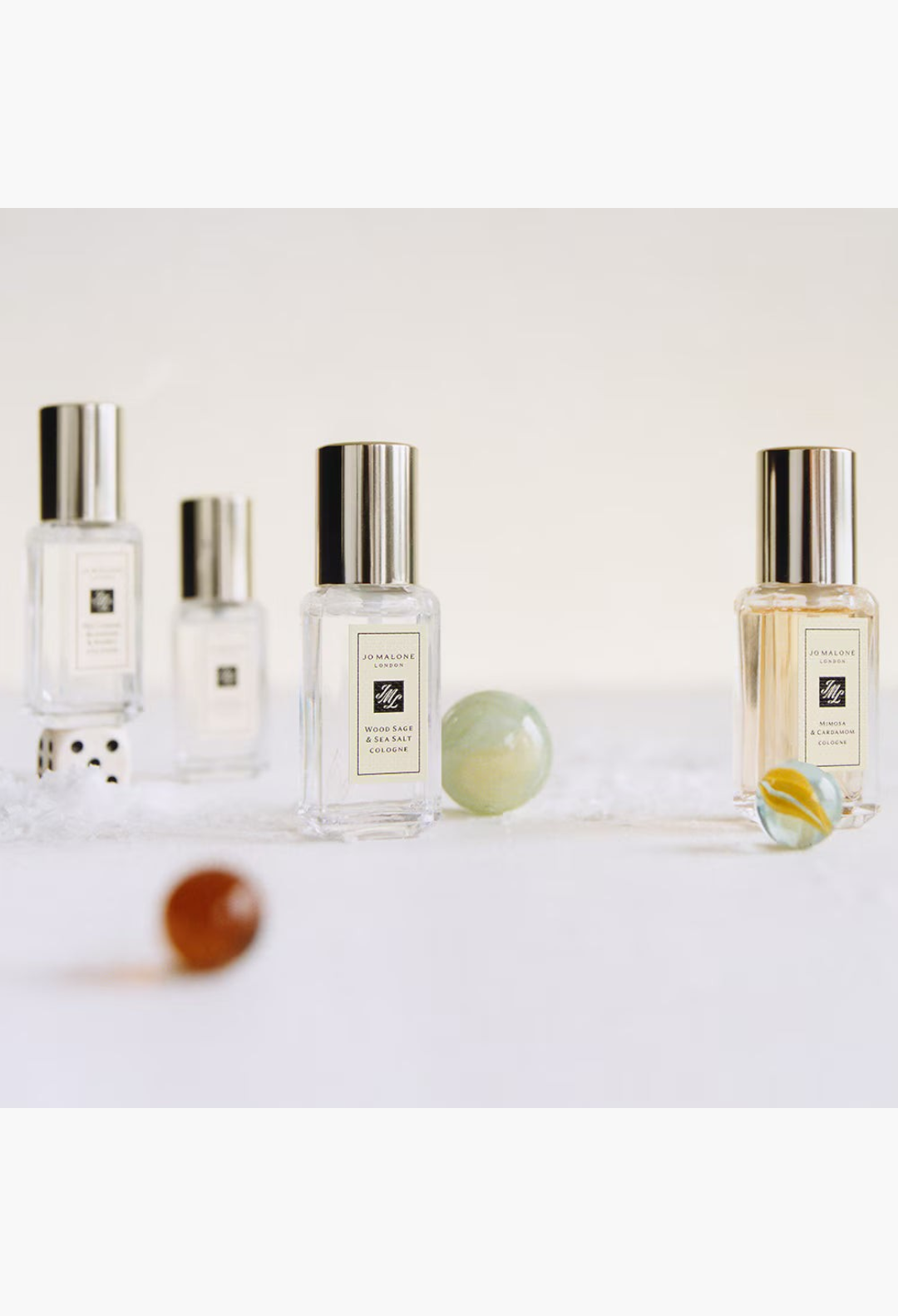 GLAM MODA collection of Jo Malone London cologne bottles with decorative dice and marble spheres on white background