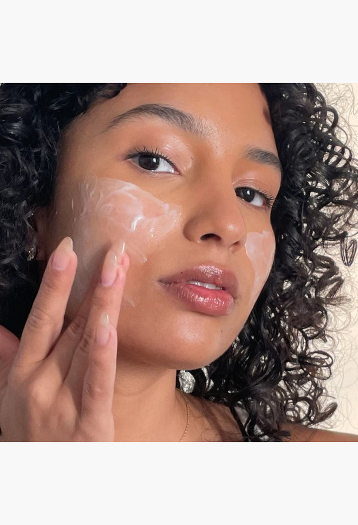 GLAM MODA goat milk moisturizing cream cleanser applied to the face of a woman with curly hair for gentle cleansing.
