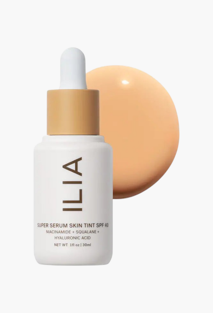 GLAM MODA ILIA Super Serum Skin Tint SPF 40 bottle with a drop of liquid foundation behind it on a white background.