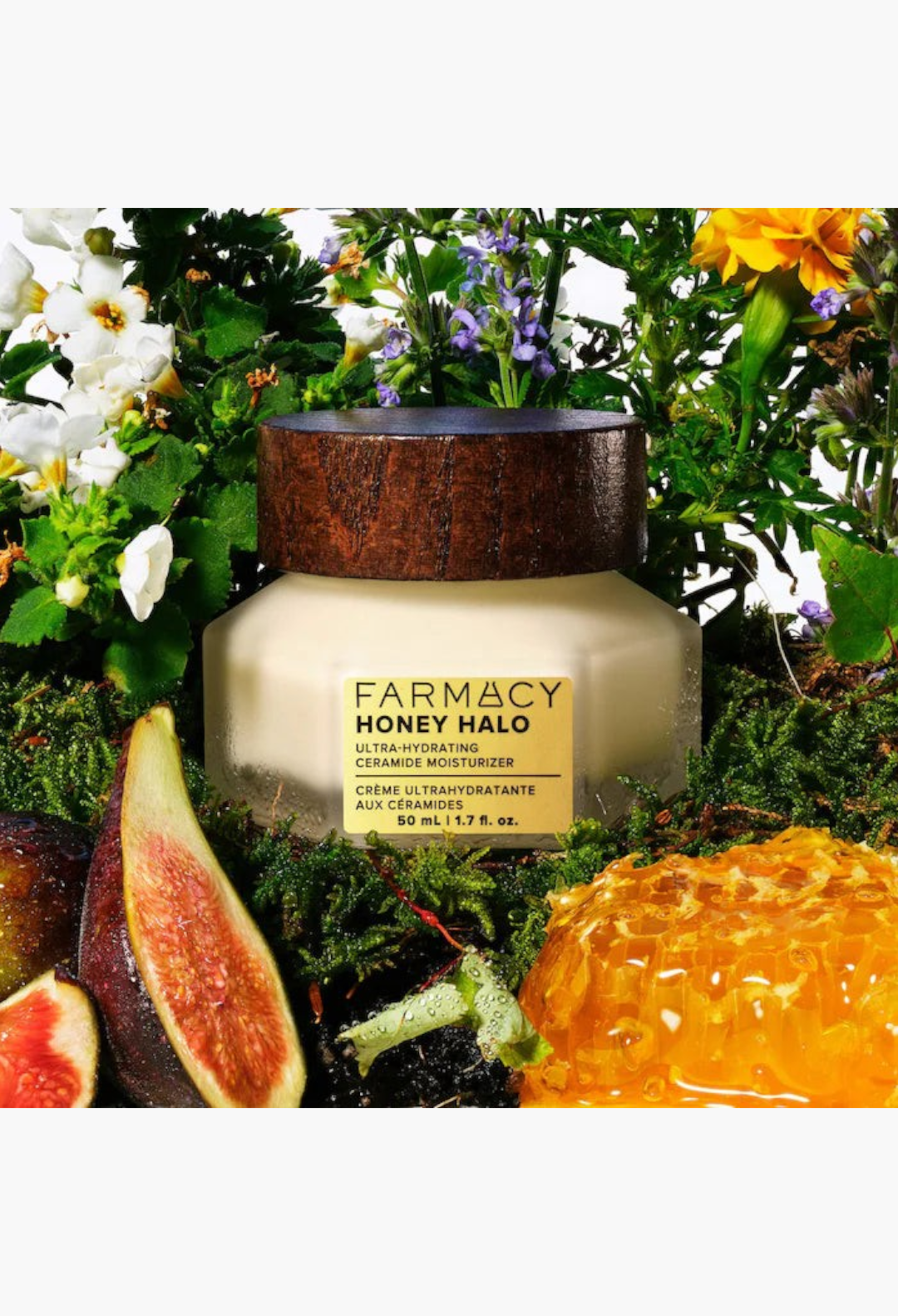 GLAM MODA Honey Halo moisturizer jar surrounded by fresh figs, honeycomb, and flowers in a natural garden setting.