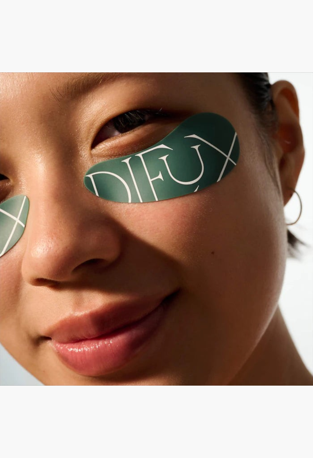 GLAM MODA reusable silicone eye masks in dark green applied under the eyes of a smiling woman for hydration.