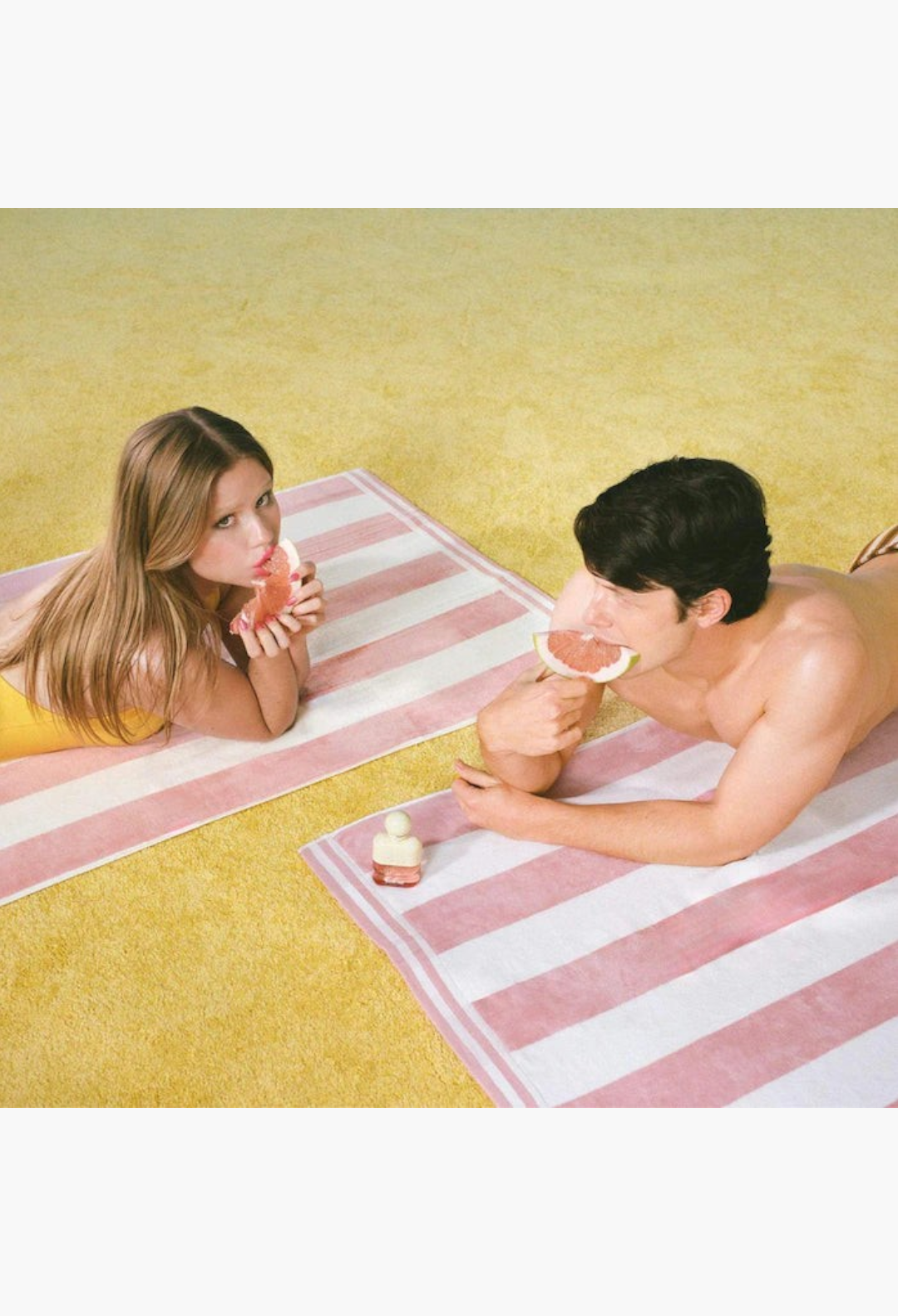 GLAM MODA Solar Drip perfume bottle on a striped beach towel with a couple eating fresh pomelo slices