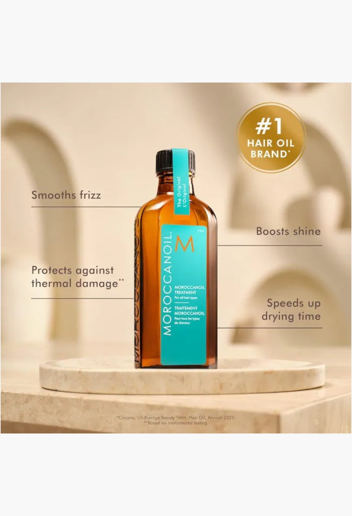 GLAM MODA Moroccanoil hair treatment bottle on a marble tray with text highlights for frizz, shine, and protection.