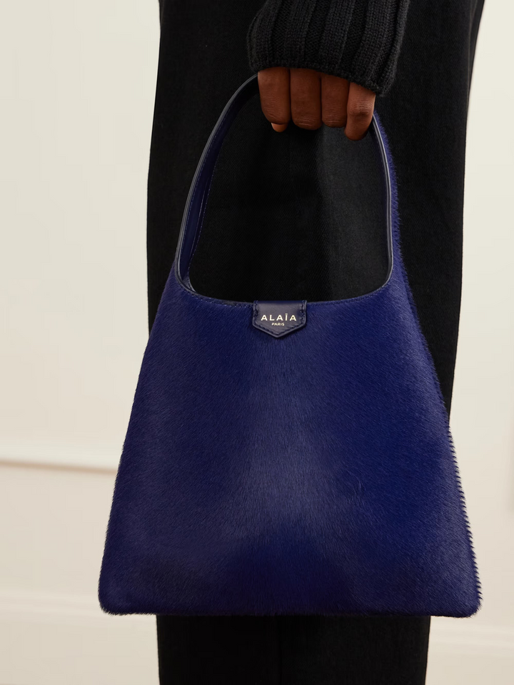 GLAM MODA Alaïa mini shoulder bag in deep blue calf hair with a leather strap and open top design held by a model